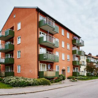 Fyravåningshus med orange fasad och gröna balkonger, ihopsittandes med trevåningshus med ljus fasad och gröna balkonger.