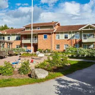 Flerbostadshus i två våningar med mixad tegelfasad och grön träfasad. Lekpark på innergården.