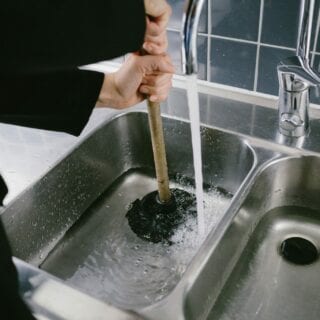 En person sätter en vaskrensare över hålet i diskhon som är fylld med lite vatten.