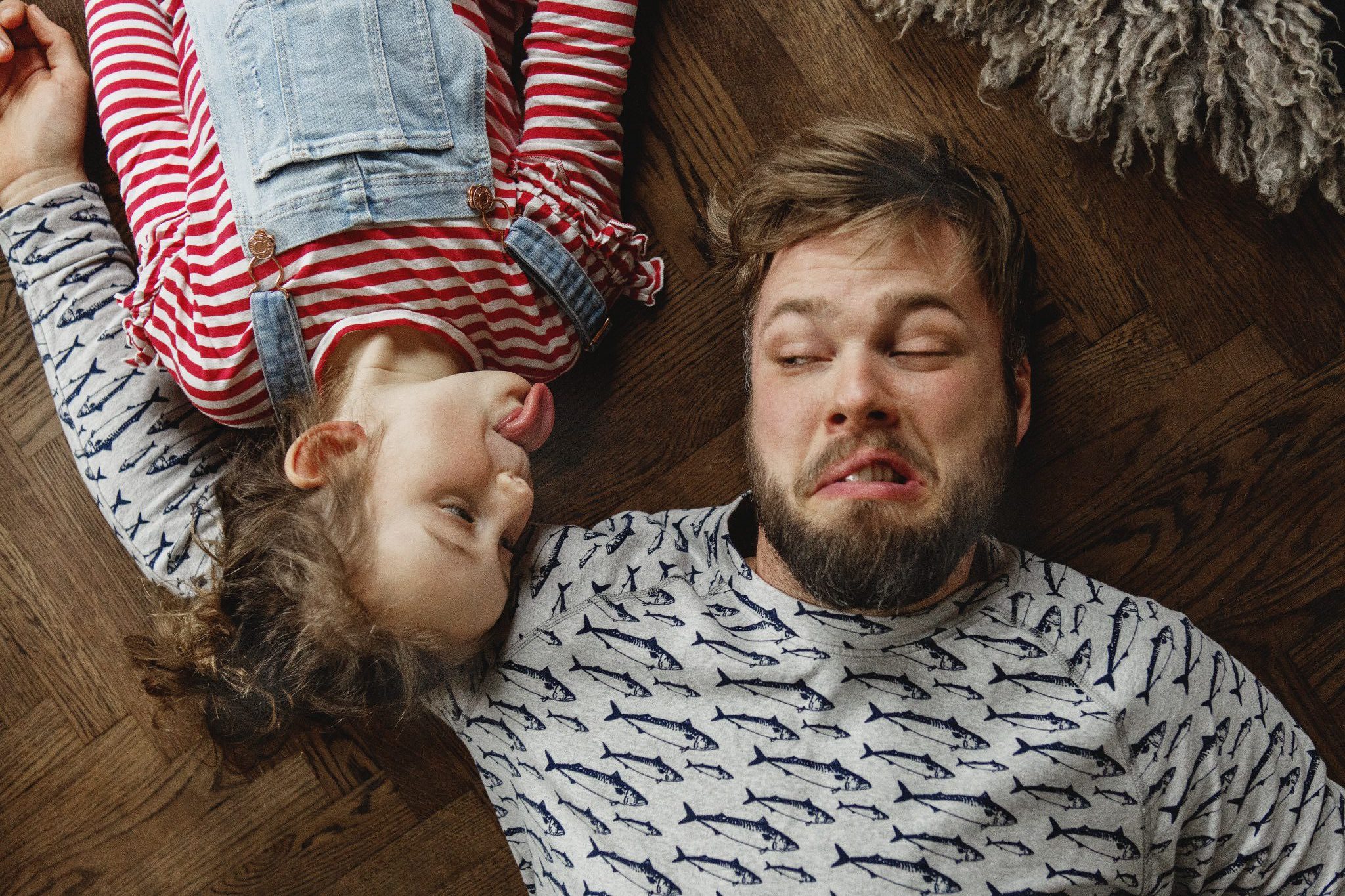Pappa och dotter liggandes på golvet, dottern lipar åt pappan, som gör en grimas.