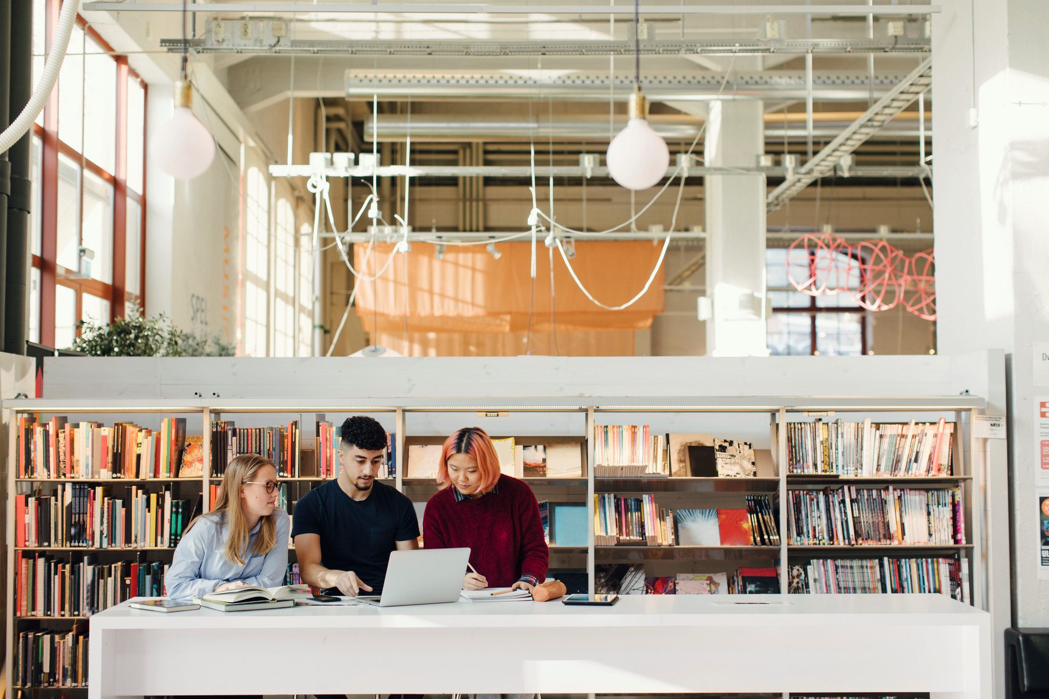 Tre studenter i ett bibliotek tittar på en dator