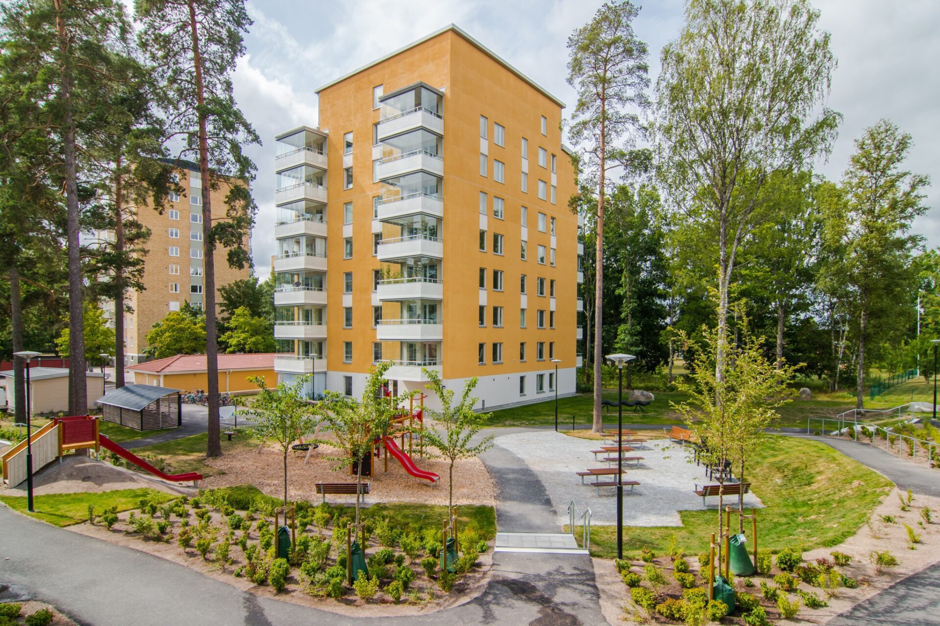 Punkthus i sju våningar med gul putsad fasad och inglasade balkonger. Innergård med lekpark.