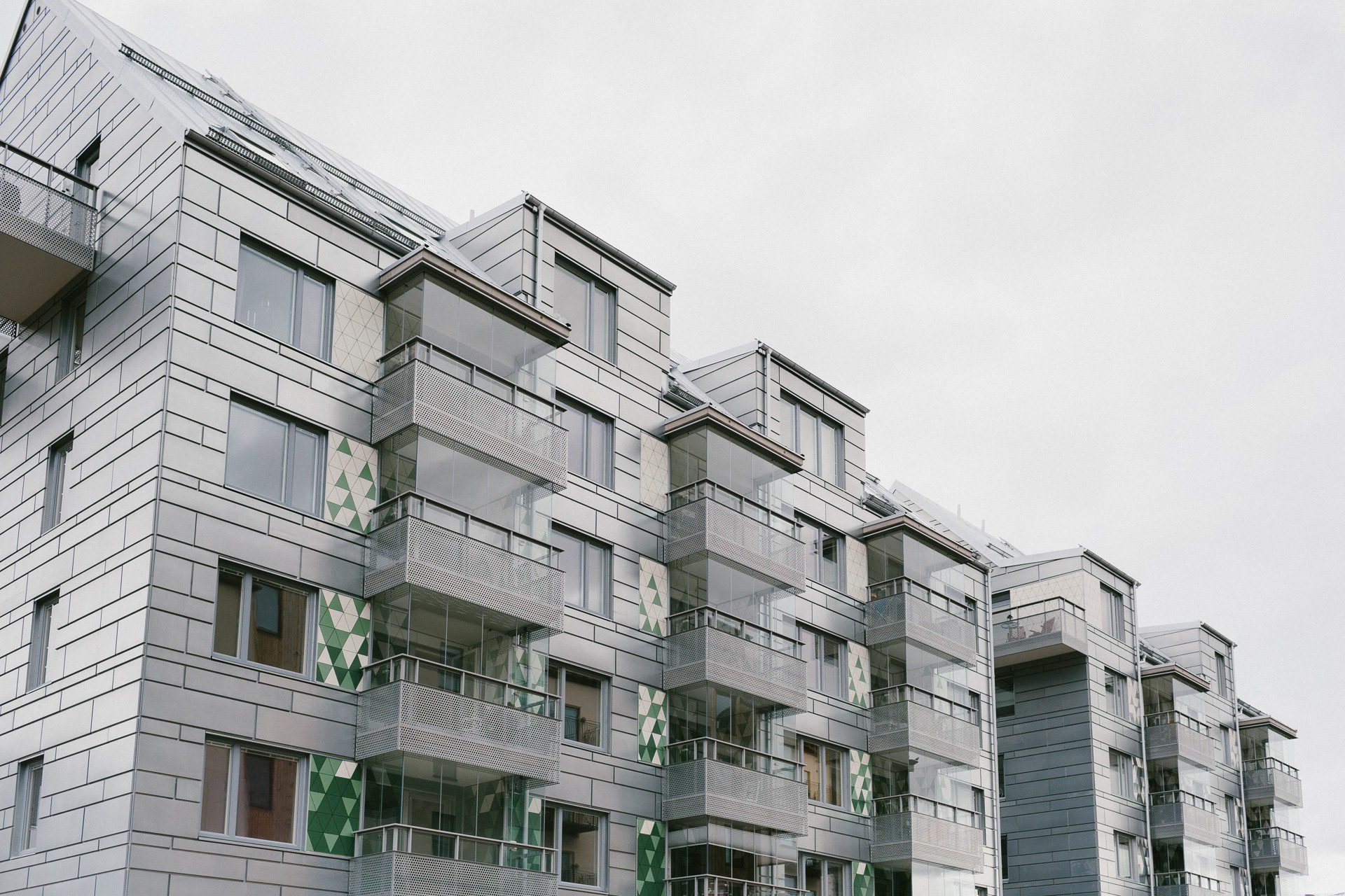 Flerfamiljshus med silvergrå plåtfasad och inglasade balkonger