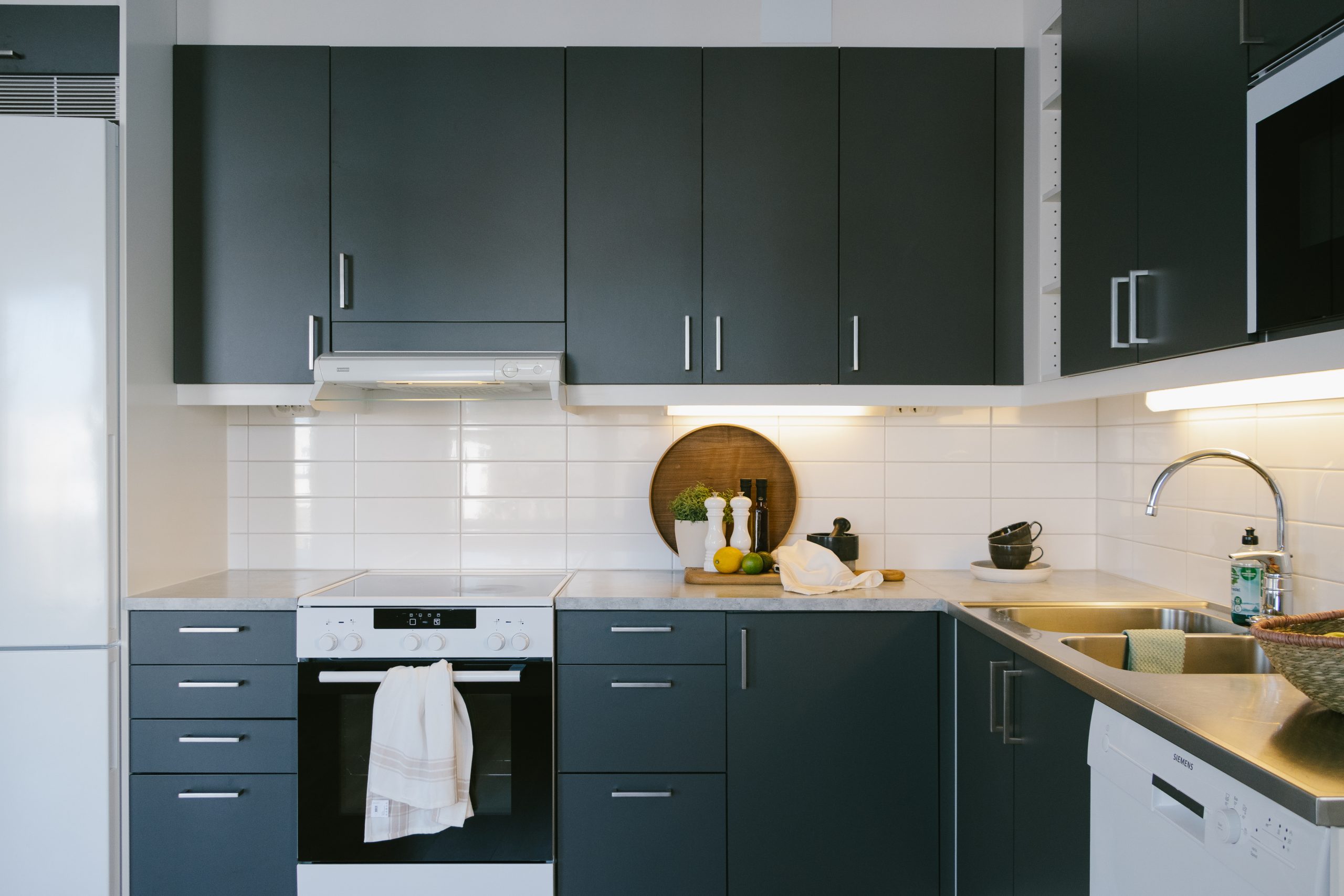 Kök med mörkgrå luckor och vitt kakel