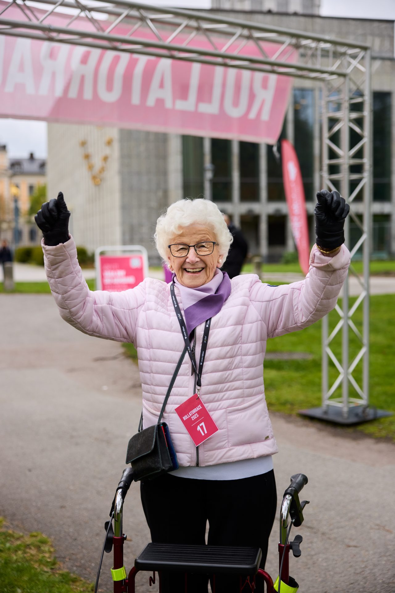 Äldre kvinna med rollator höjer armarna i en segergest